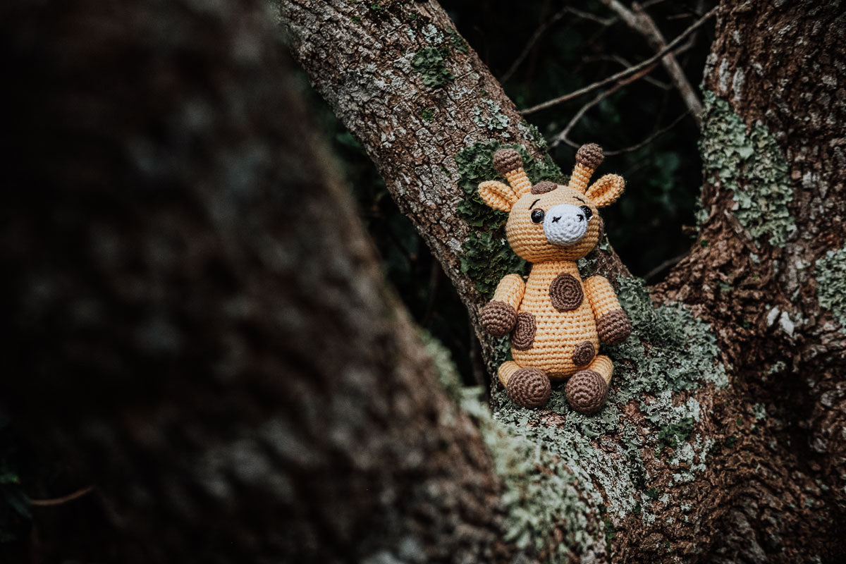 hand crochet giraffe sitting on a tree branch