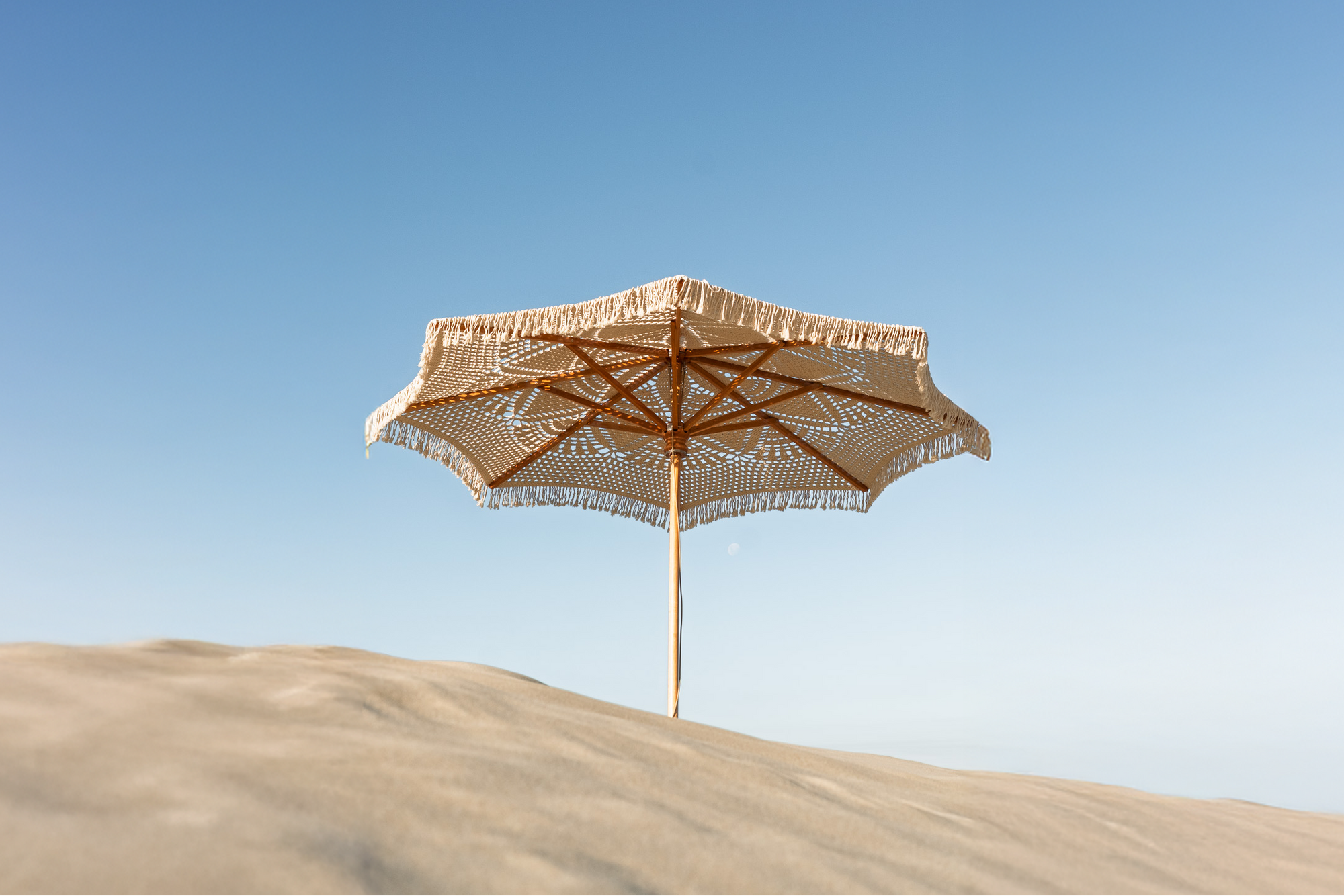 Hand crocheted parasol/umbrella with wooden pole on a sand dune with a clear blue sky